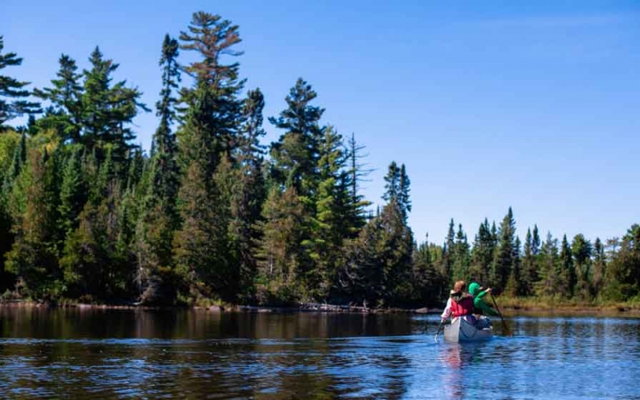 a canoe is paddled by outward bound students on calm waters beside tall green trees